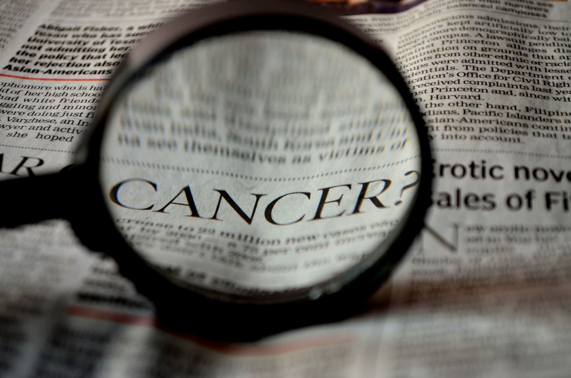 newspaper with word cancer under magnifying glass