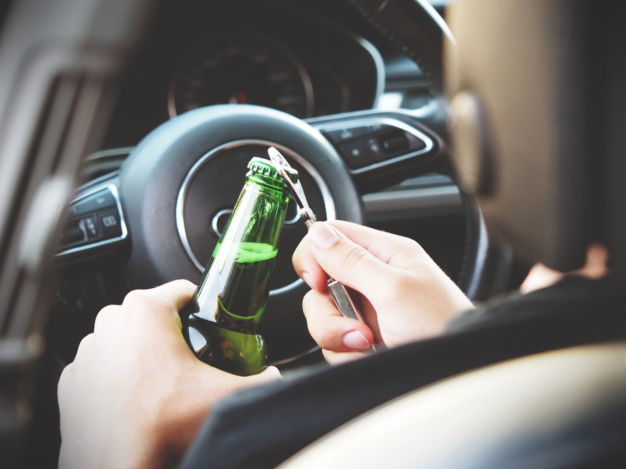 Person opening beer behind the wheel of a car