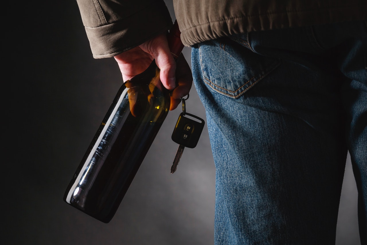 Person holding car keys and bottle of alcohol