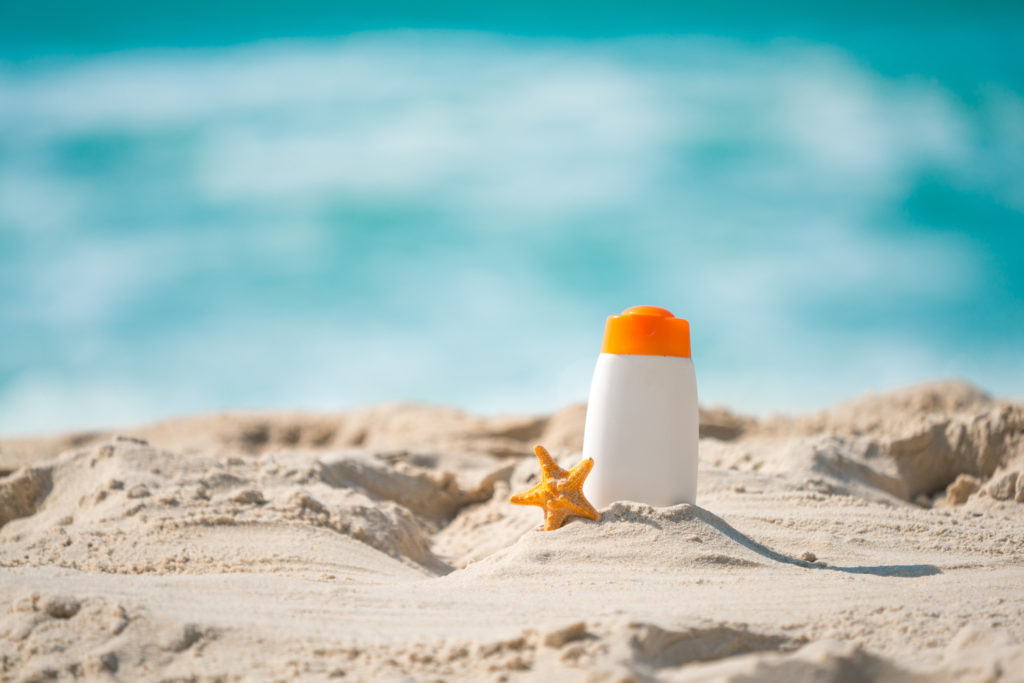 Bottle of sunscreen lotion and starfish on tropical beach, Beach accessories and summer concept