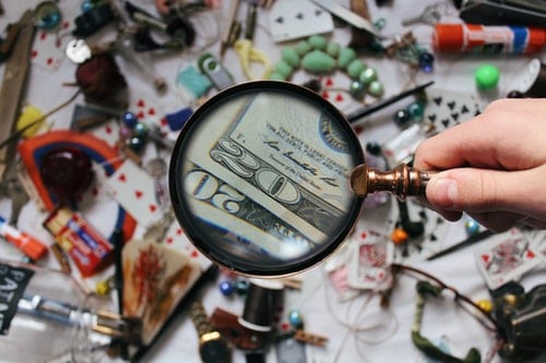 magnifying glass showing two twenty dollar bills against a blurry background of haphazardly places items and junk