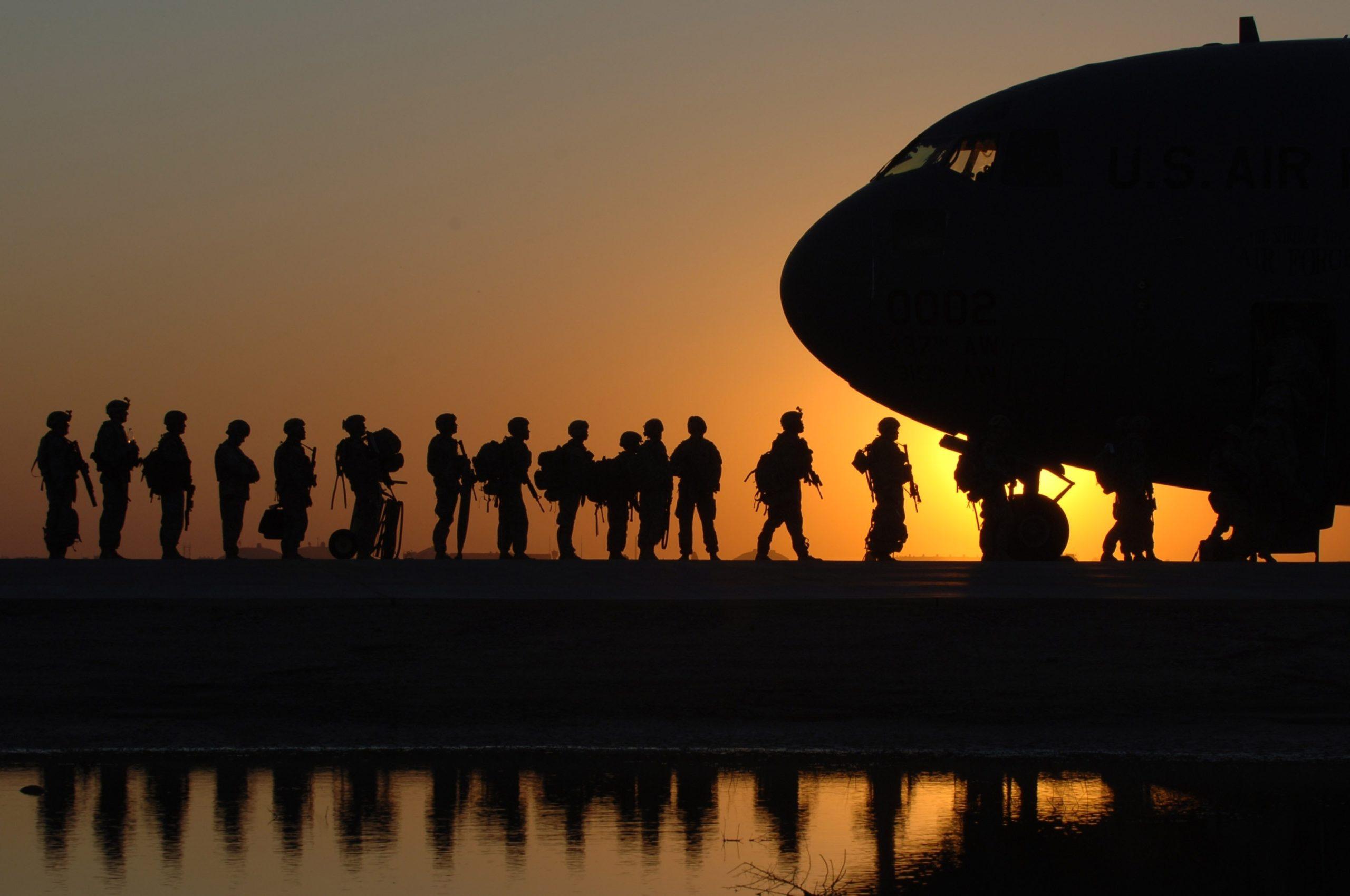 Soldiers lined up in front of a plane, against the sunset