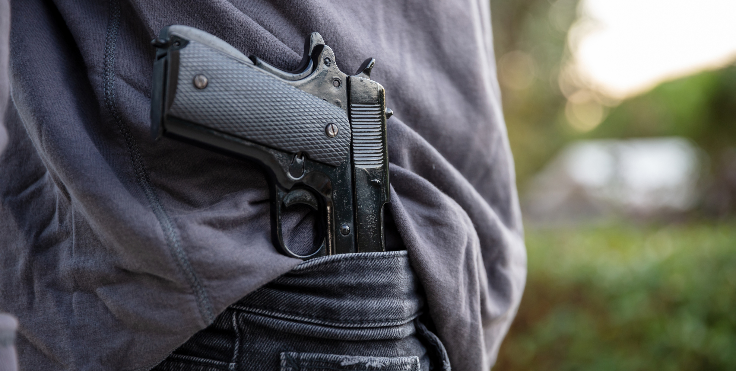 Hombre armado que lleva una pistola en la cintura de sus jeans, desenfoca el fondo de la naturaleza al aire libre. Concepto de amenaza, violencia y peligro.